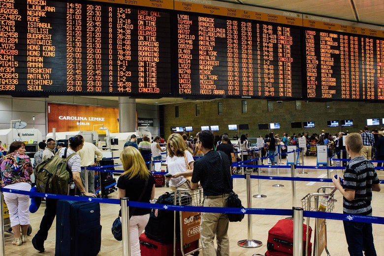 People stand in line below a departures and arrivals board.